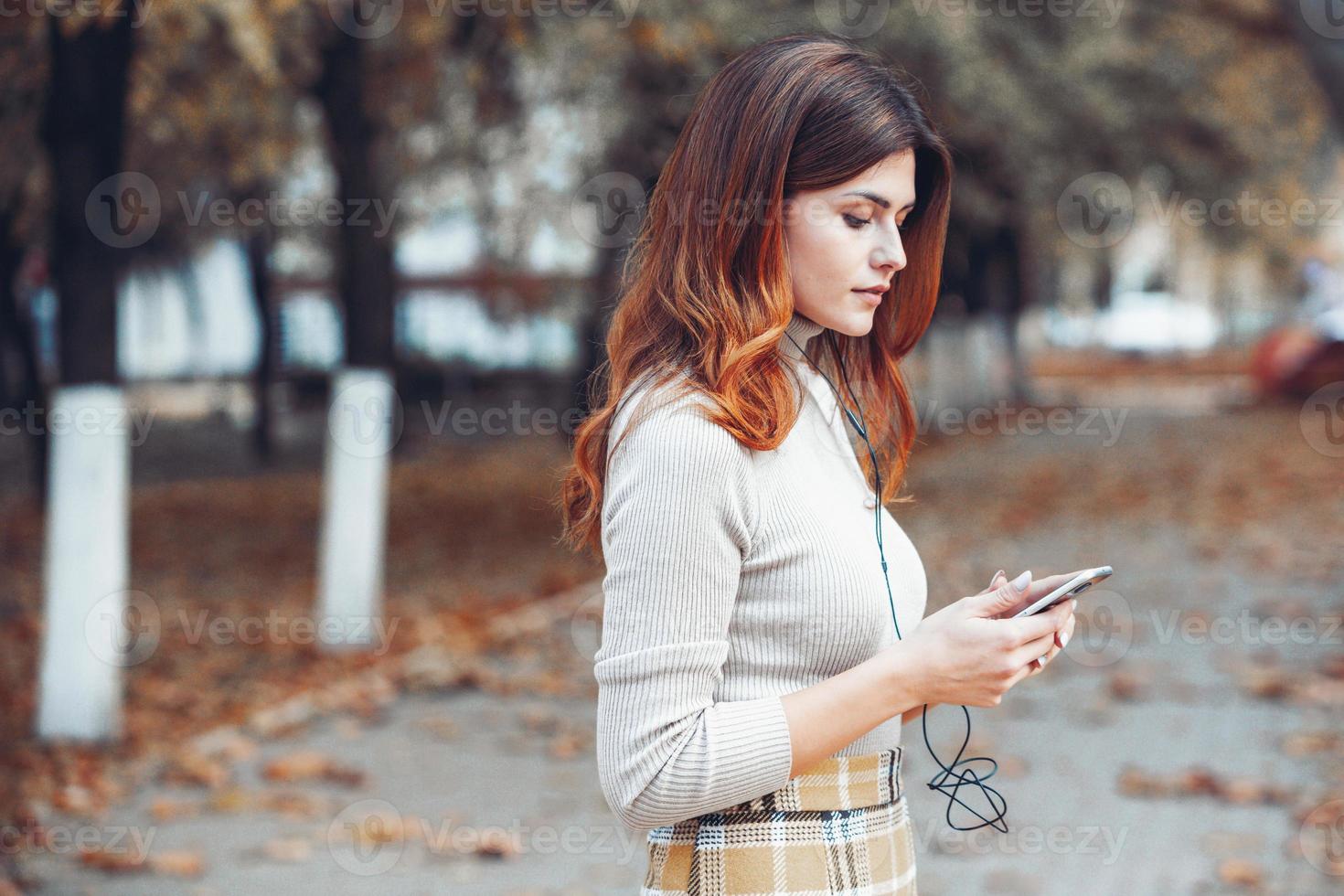 image de belle femme élégante tenant un téléphone portable. jeune fille européenne debout dans la rue et utilisant un téléphone portable. femme écoutant de la musique avec le téléphone et s'amusant. notion d'internet mobile. photo