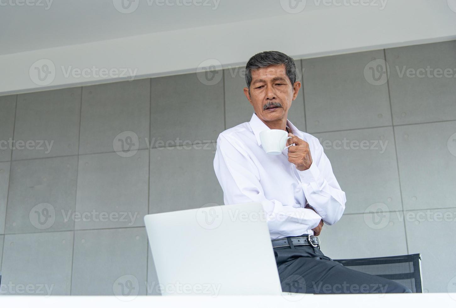 vieil homme d'affaires asiatique avec une chemise blanche travaillant et buvant du café dans la salle de réunion au bureau photo