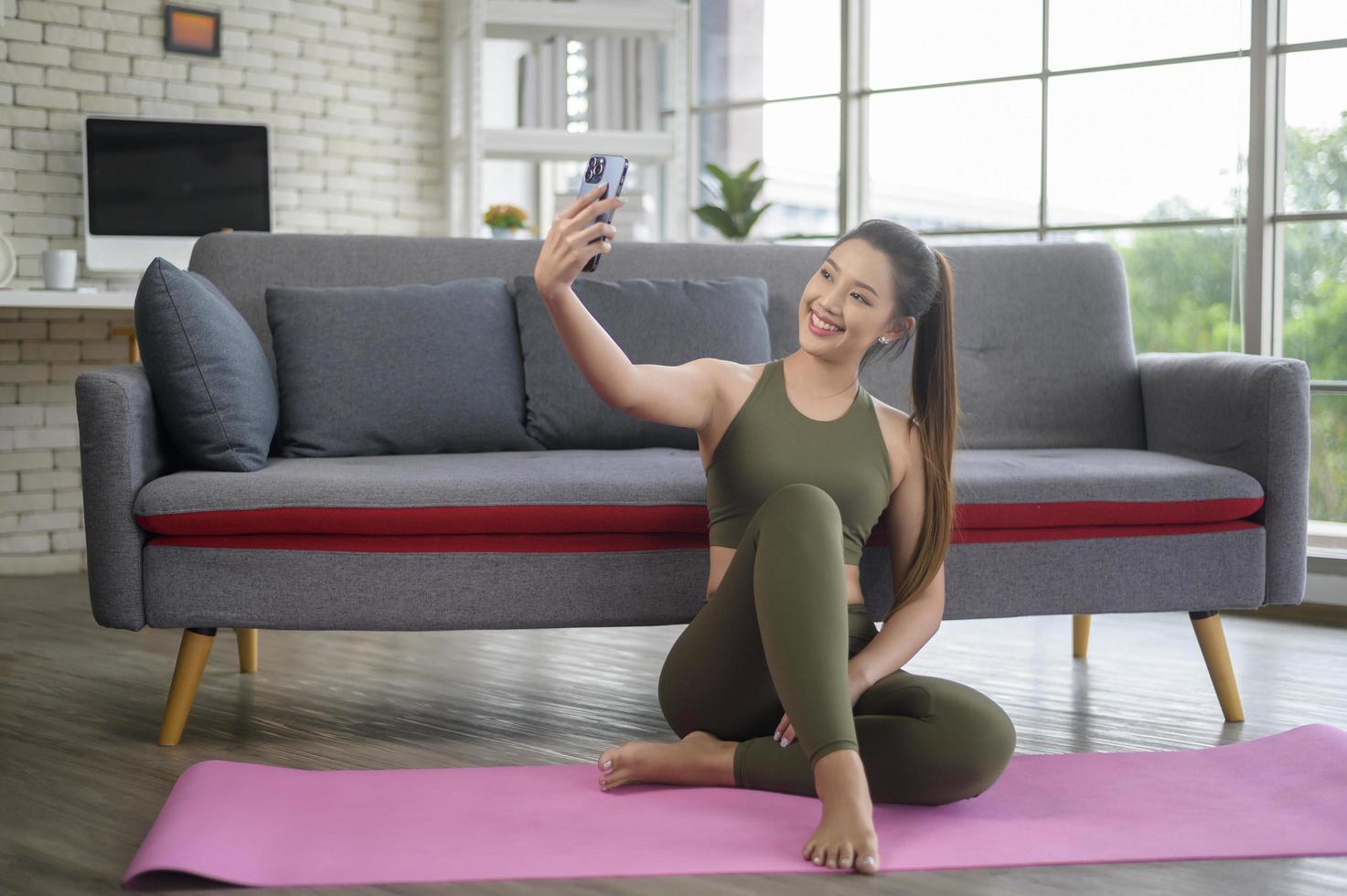 jeune femme de remise en forme en vêtements de sport utilisant un téléphone intelligent tout en faisant de l'exercice à la maison, en bonne santé et modes de vie. photo