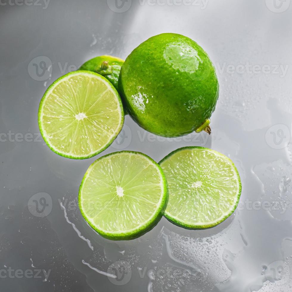 le citron vert est vierge avec la tranche de citron vert coupée montrant l'intérieur de la pulpe de citron humide sur une surface en verre transparent, reflétant les ombres du citron vert et de l'eau humide, lui donnant sa fraîcheur. photo