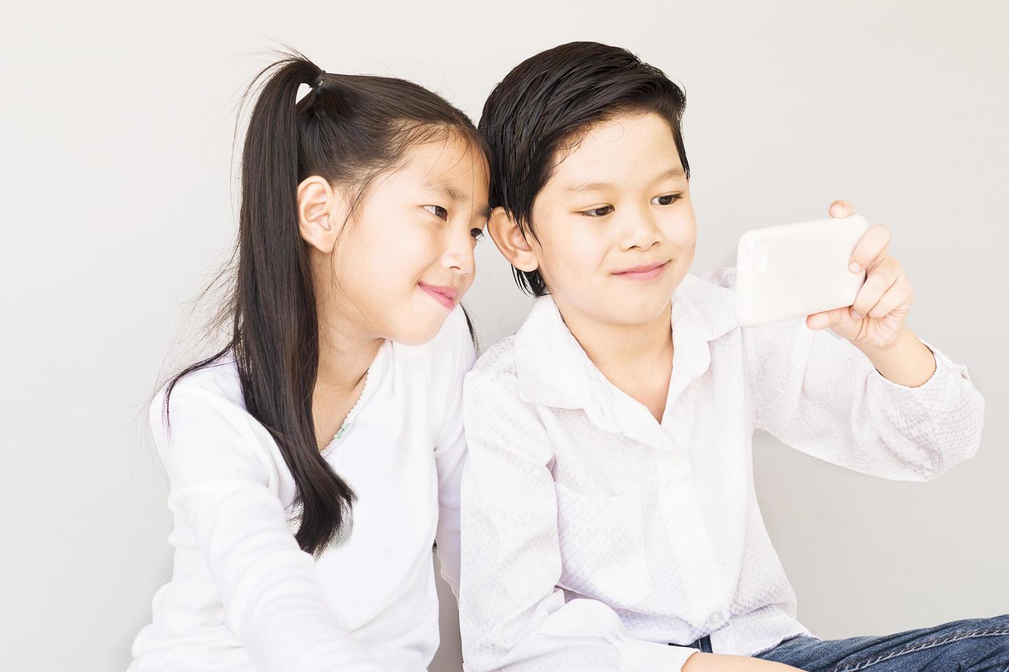 joli couple asiatique écoliers prennent selfie, 7 et 10 ans, sur fond gris photo