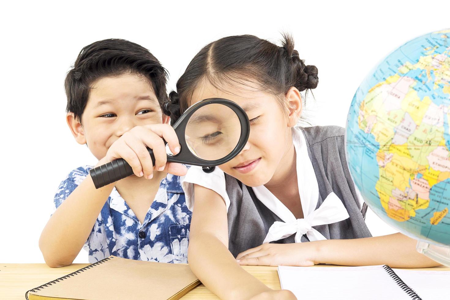 les enfants asiatiques étudient le globe à l'aide d'une loupe sur fond blanc photo