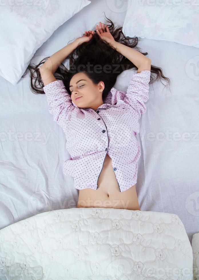 fille dort dans un lit blanc à la maison. jeune femme dormant en vêtements de nuit sur le linge blanc dans son lit à la maison, vue de dessus. photo