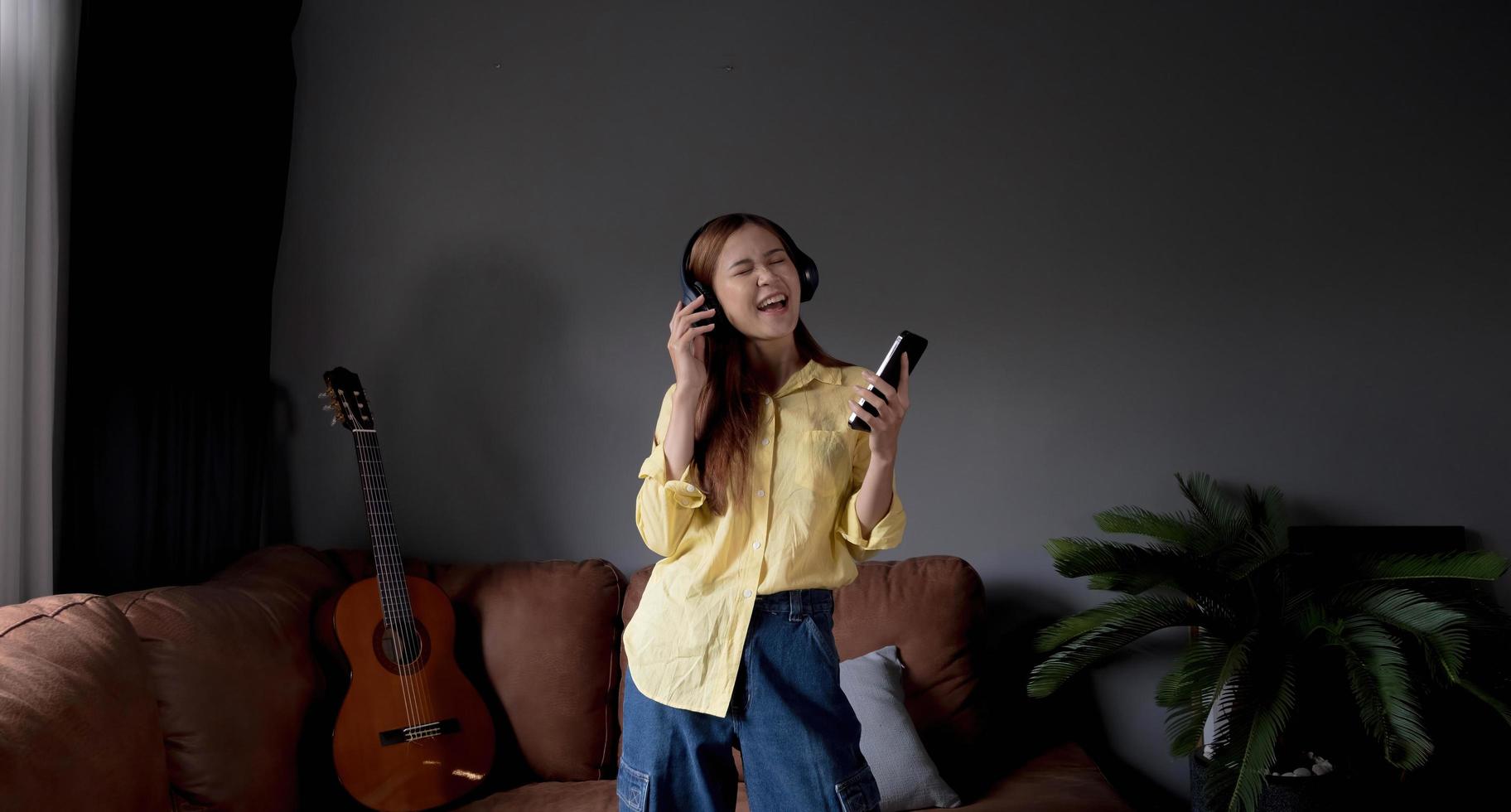 jeune femme asiatique écoutant de la musique sur un canapé dans le salon à la maison. femme asiatique heureuse utilisant un smartphone mobile, portant un casque photo