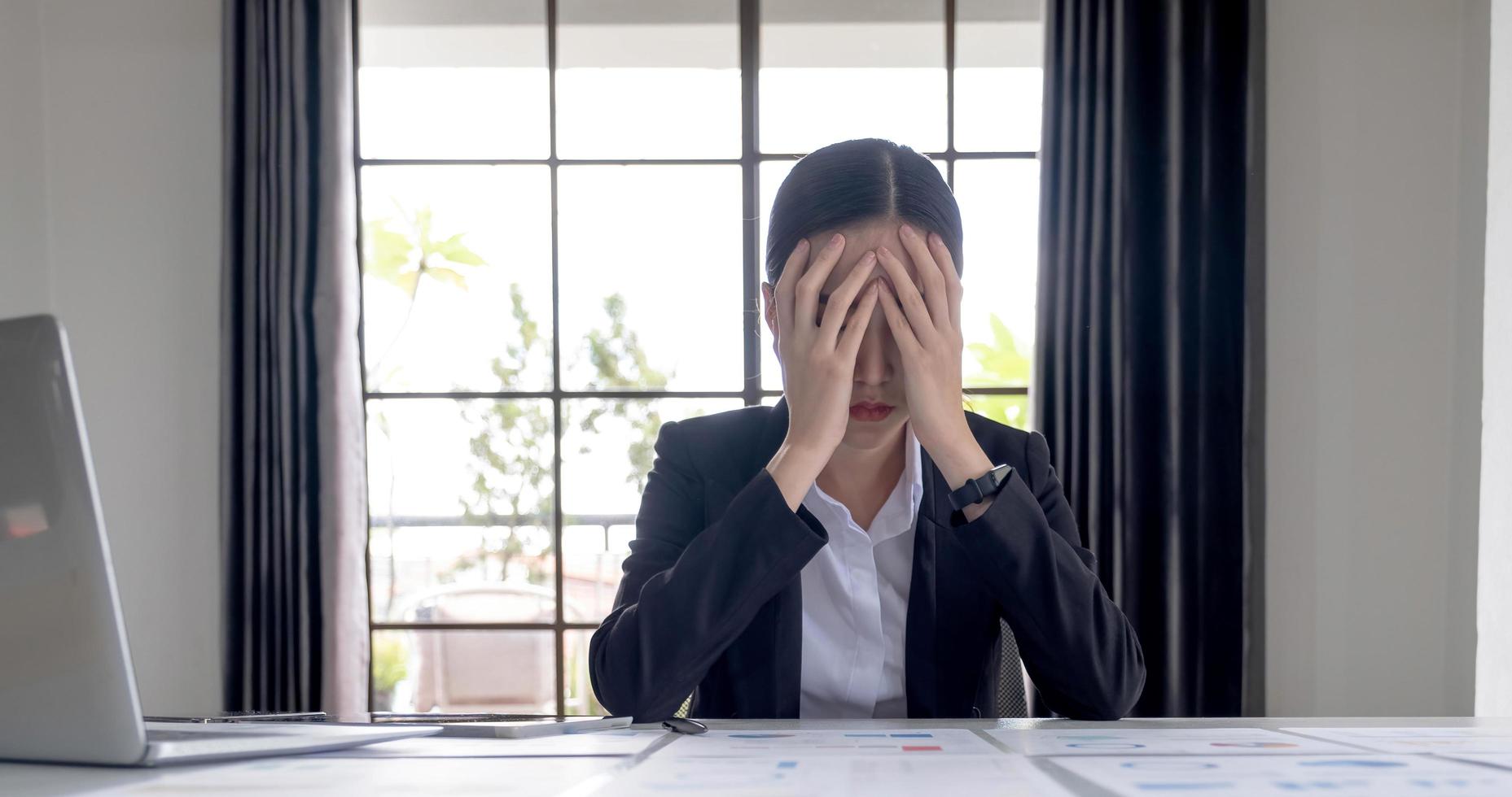 jeune femme d'affaires asiatique travaillant sur une tablette, est stressée a mal à la tête et pense dur au bureau. photo