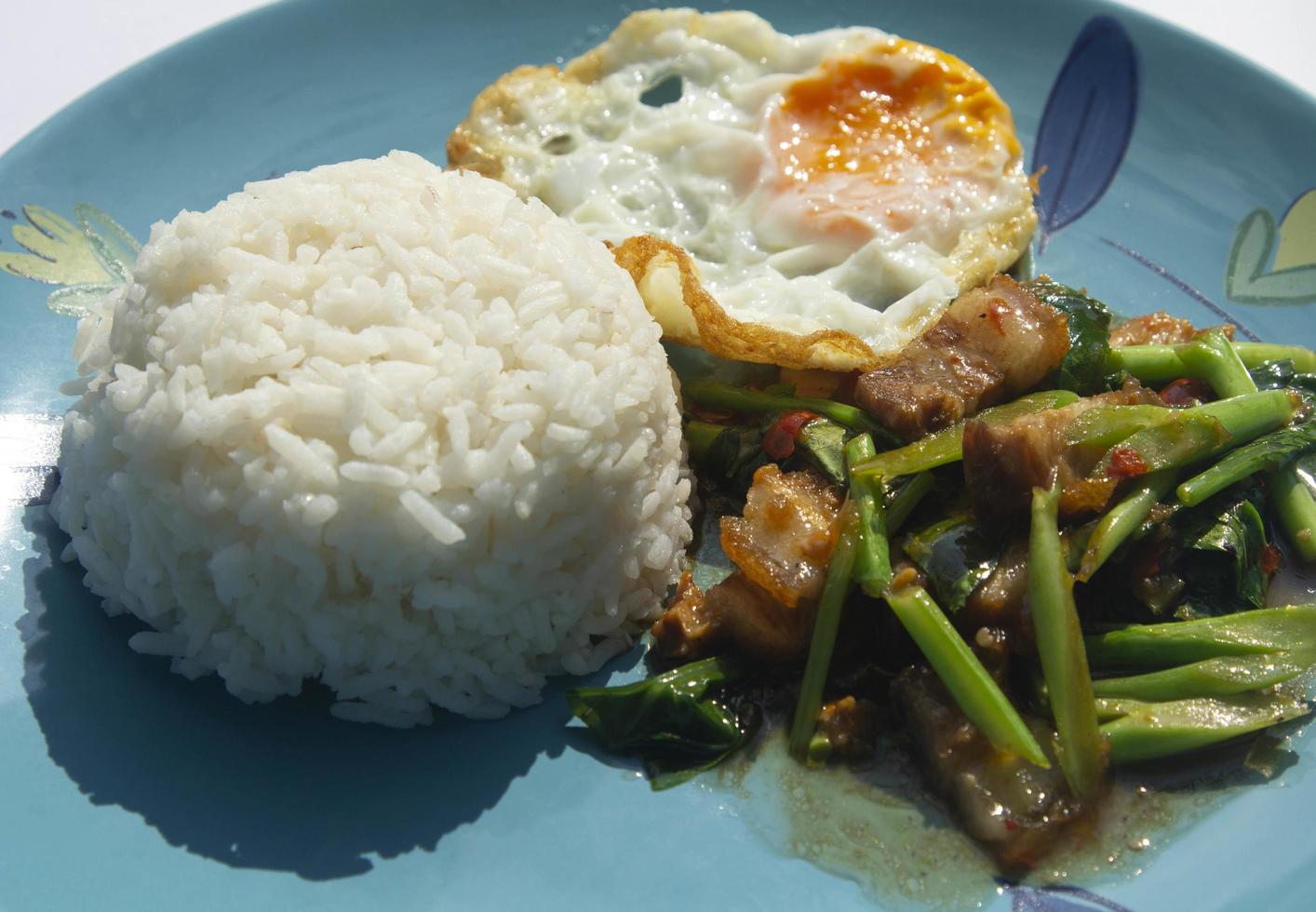 Le chou frisé au porc croustillant - l'œuf frit est un plat thaïlandais épicé et délicieux facile à trouver en Thaïlande. servi dans un plat bleu clair sous le chaud soleil du matin - c'est de la restauration rapide. photo