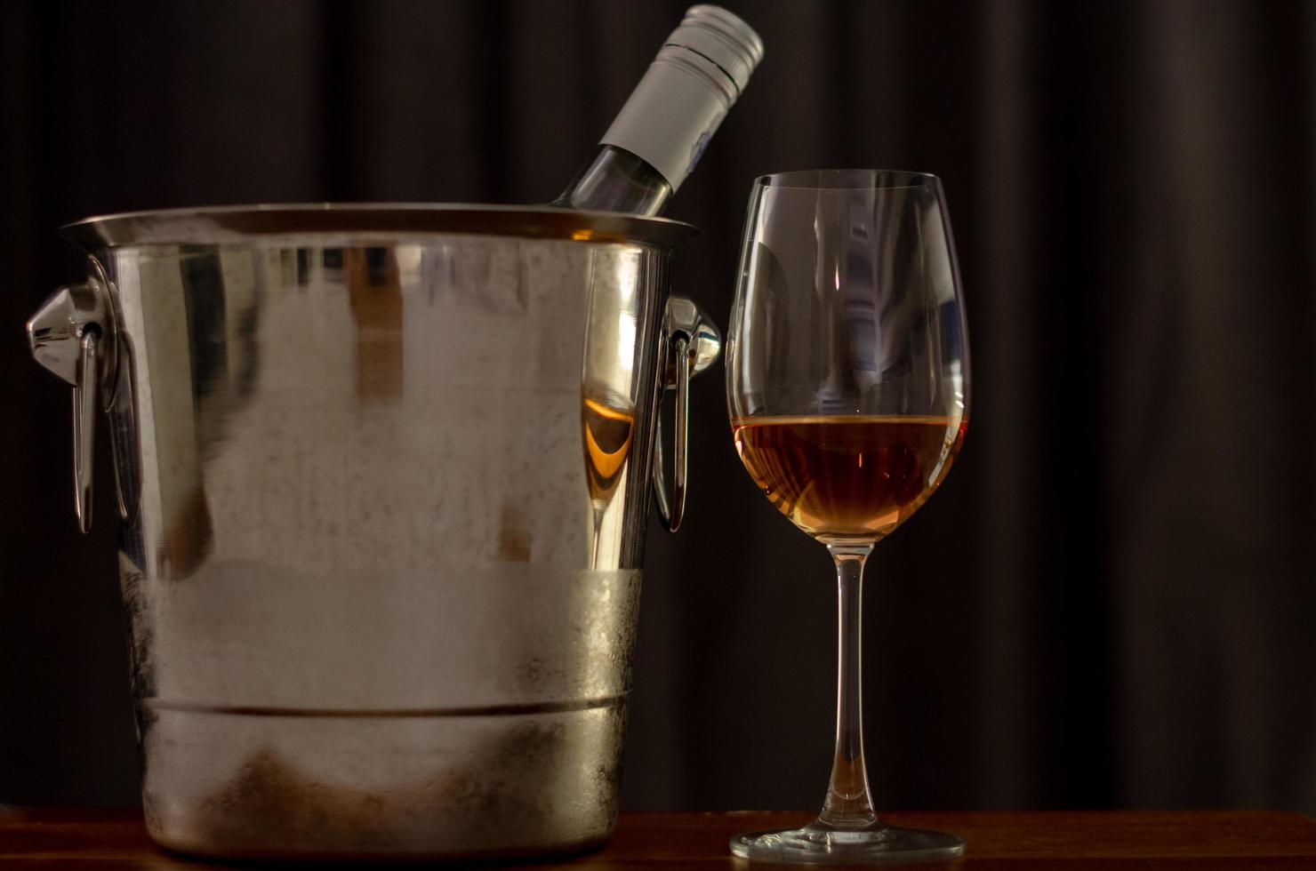 un verre de vin rosé sur une table en bois avec une bouteille dans un seau de refroidisseur de vin. photo