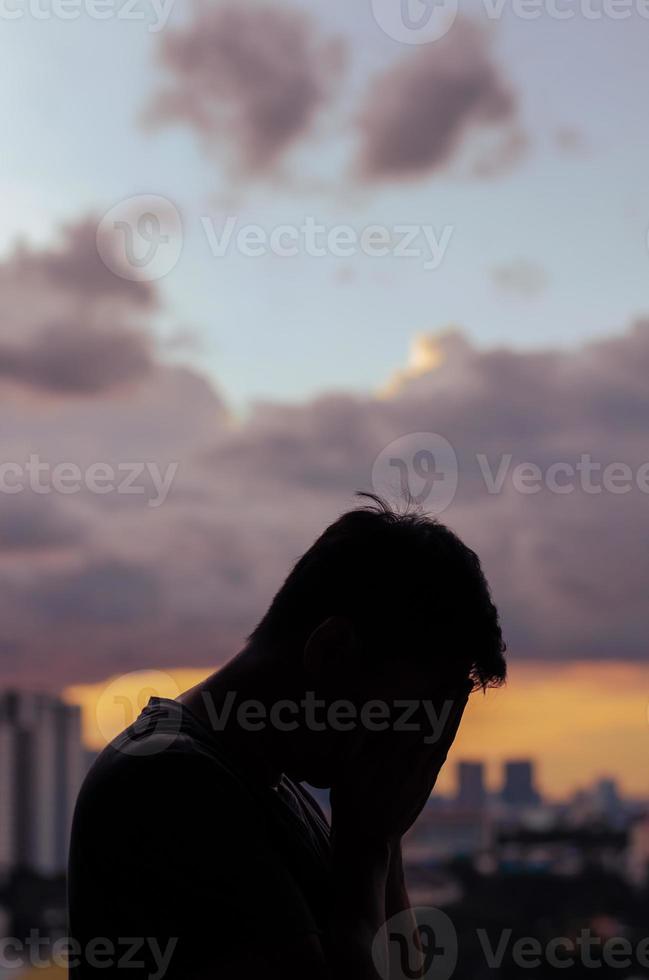 silhouette d'homme déprimé en pleurs avec ciel nuageux et fond de ville. photo