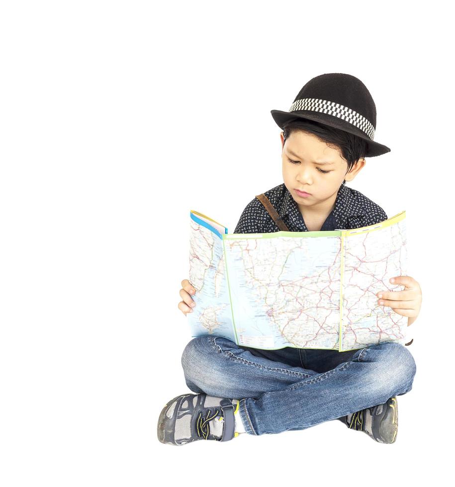 Un garçon voyageur asiatique de 7 ans est assis avec bonheur et regarde une carte tout en pointant son index isolé sur blanc photo