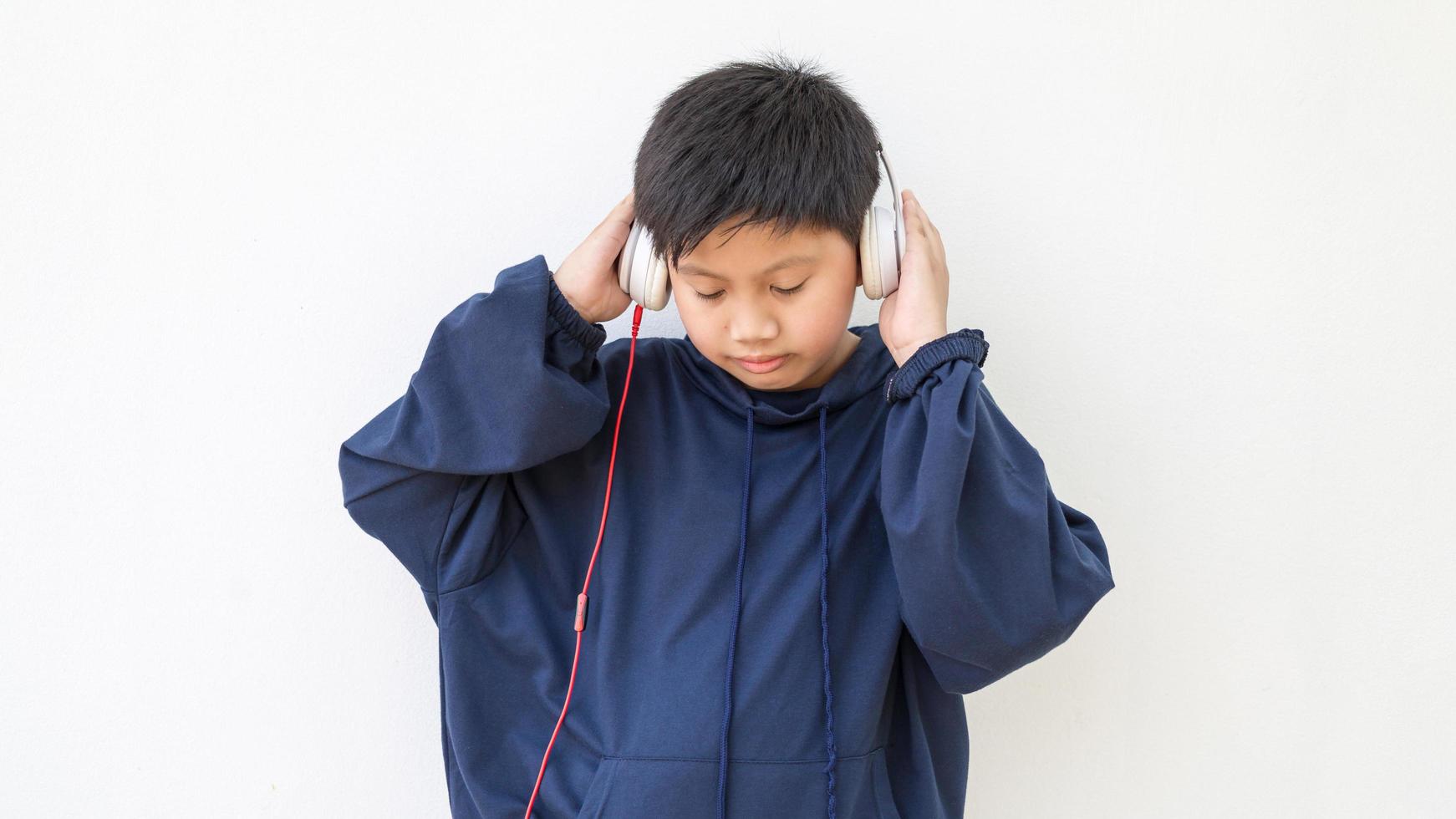 mignon garçon asiatique dans un sweat à capuche posant debout souriant détendu et heureux d'écouter de la musique avec des écouteurs. portrait émotionnel d'un jeune garçon appréciant la musique photo
