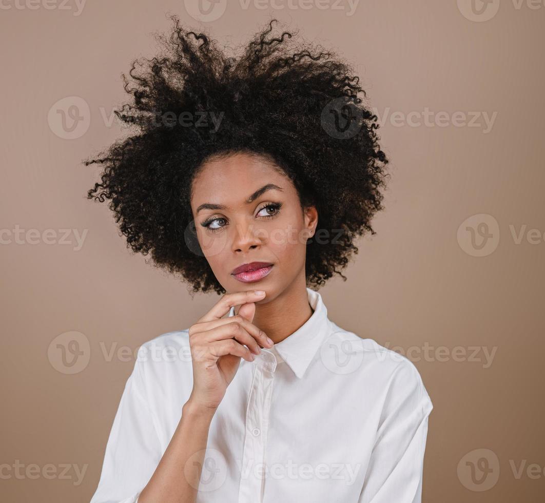 gros plan d'une jeune femme afro latine pensant. joie, positif et amour. beaux cheveux de style africain. fond de studio pastel. photo