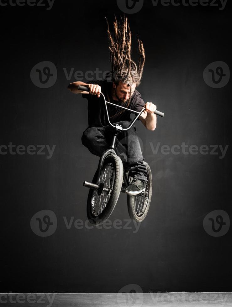 jeune homme avec des dreadlocks sautant sur son vélo bmx. photo