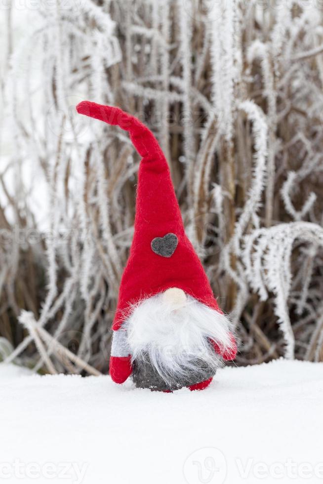 un petit jouet assis dans la neige en vêtements rouges photo