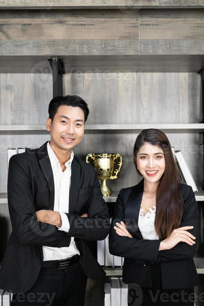 souriant jeune homme d'affaires et femme d'affaires portent un costume bras croisés sur fond de bureau moderne, entreprise prospère photo