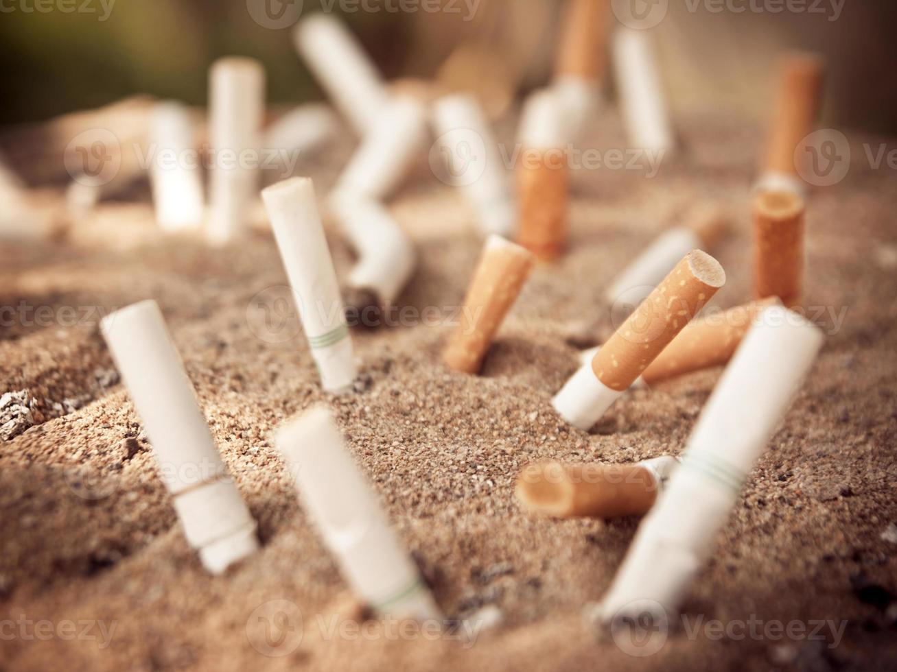 beaucoup de cigarettes brûlées sur cendrier et sable photo