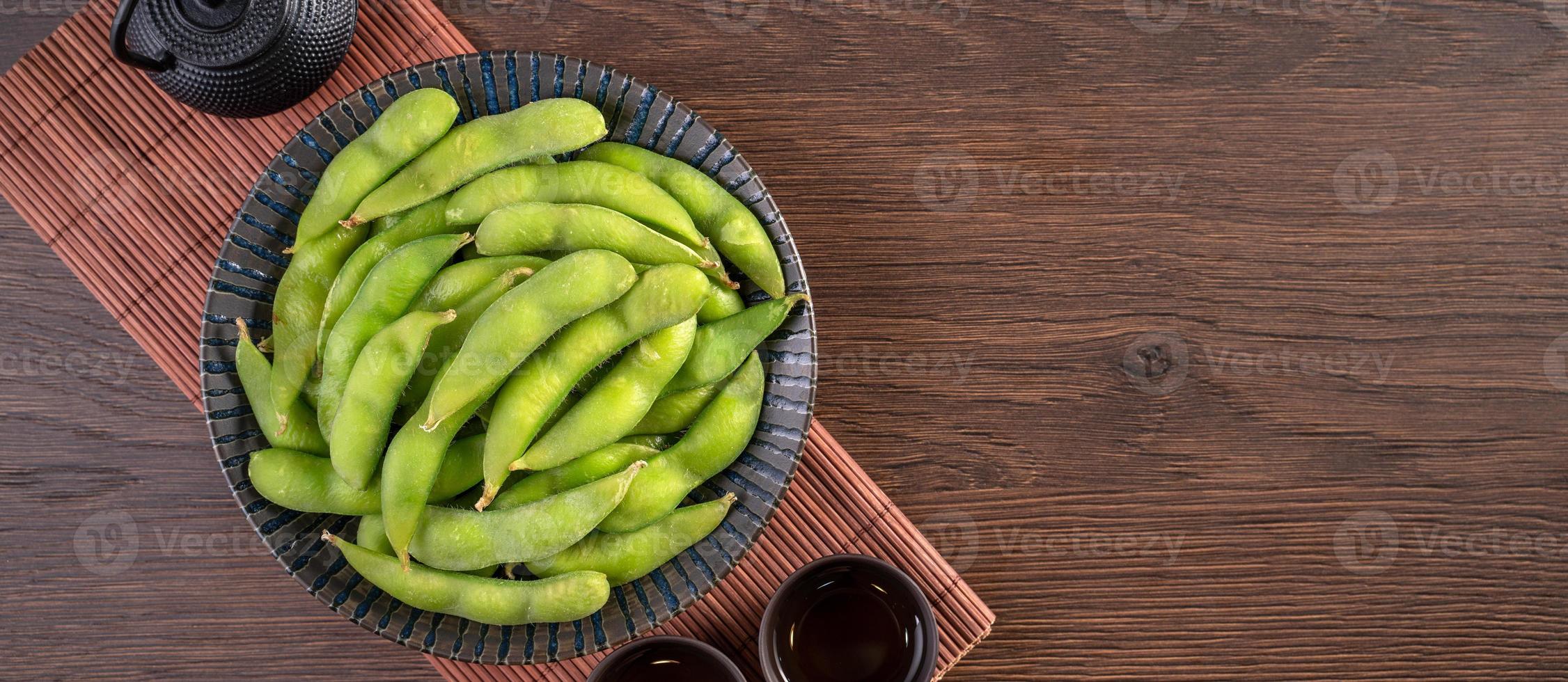 edamame bouilli frais cuit dans une assiette sur un plateau en bois et fond de table, concept d'aliments protéinés sains. photo