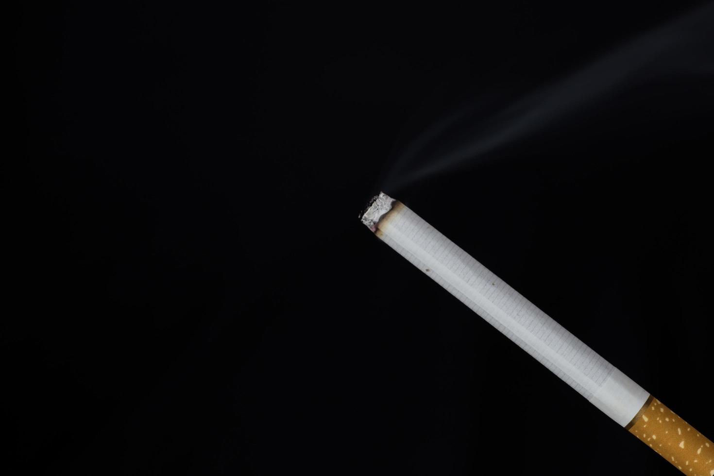 cigarette allumée avec de la fumée sur fond noir photo