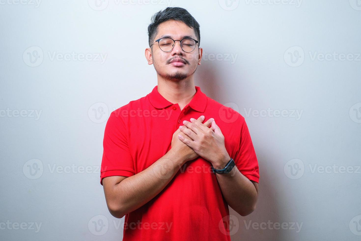 portrait d'un homme asiatique sympathique portant une chemise décontractée les yeux fermés, souriant et touchant les sentiments cardiaques photo