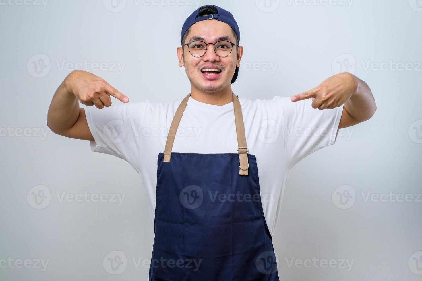 barista asiatique joyeux et sympathique portant un tablier pointant les doigts vers le bas et souriant comme montrant de la publicité avec annonce photo