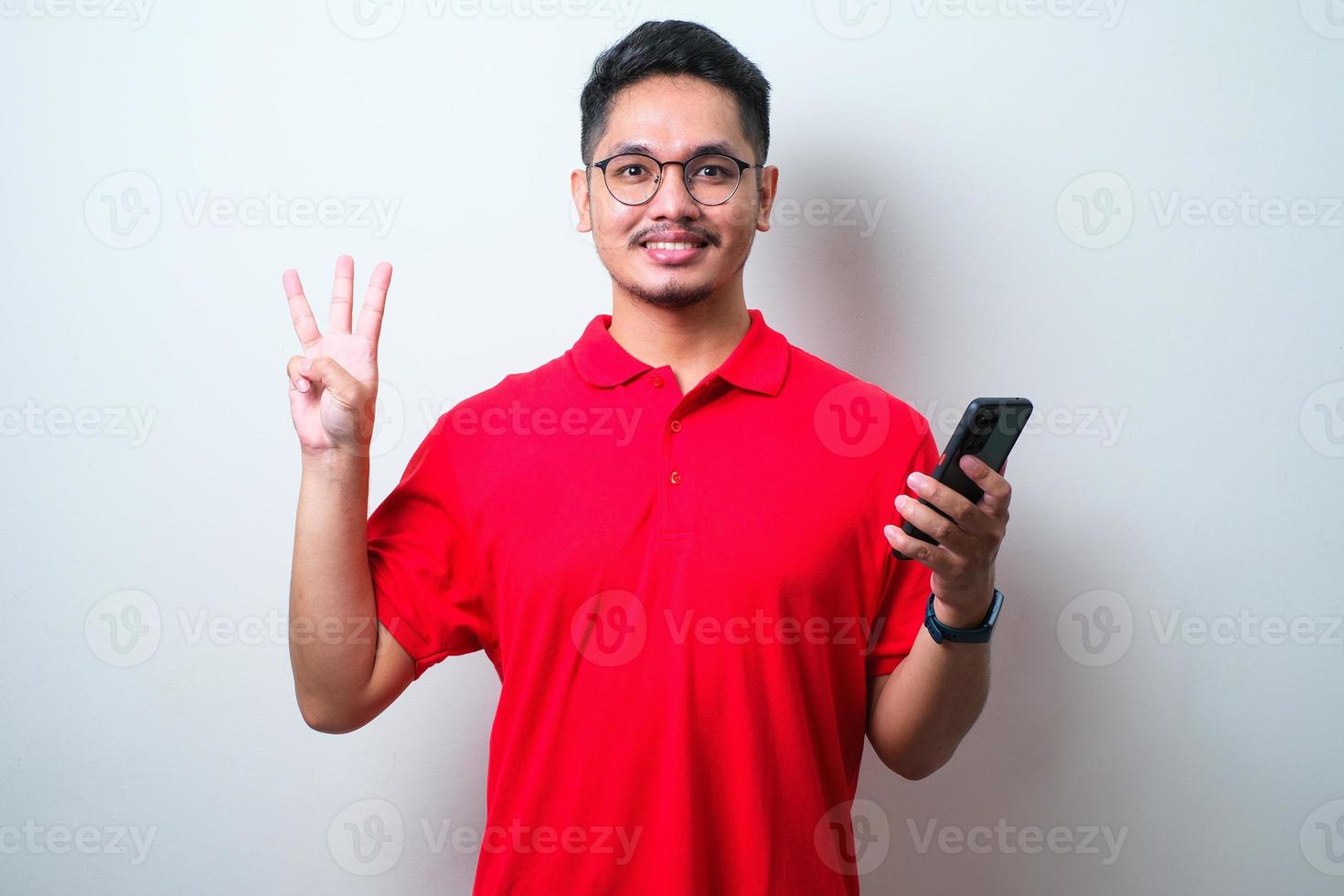 jeune bel asiatique portant une chemise décontractée et des lunettes tenant un smartphone et pointant vers le haut avec les doigts numéro trois tout en souriant confiant et heureux photo