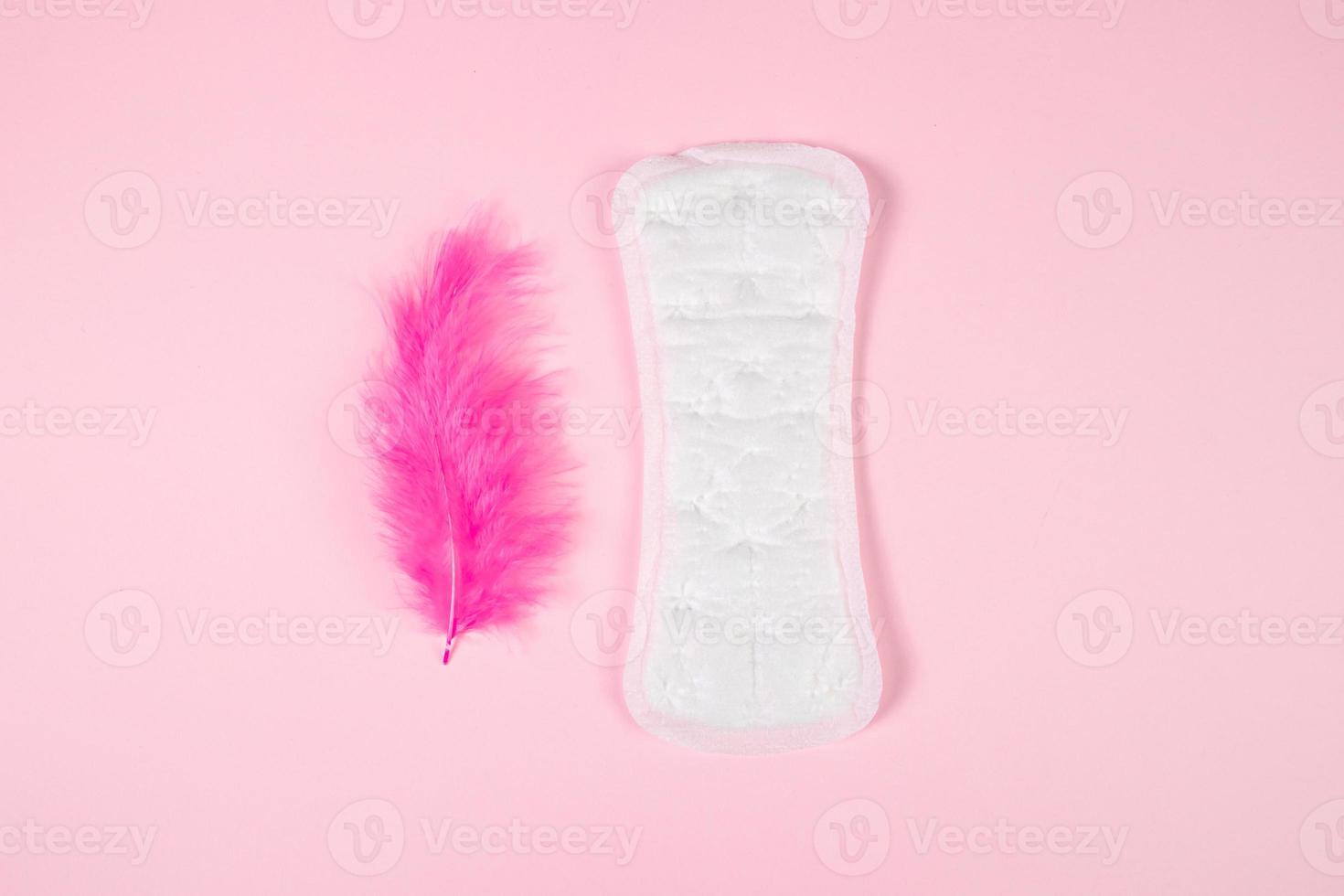 serviette hygiénique et plume rose sur fond coloré. produit d'hygiène féminine quotidien. photo