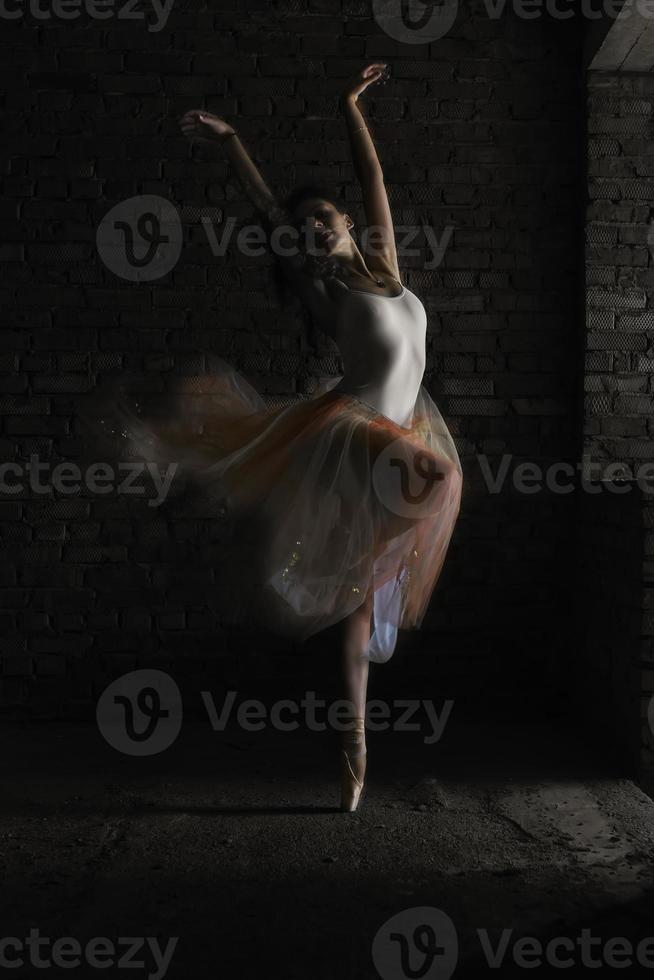 une charmante ballerine en body pose des éléments de ballet dans une coiffe dans un studio photo