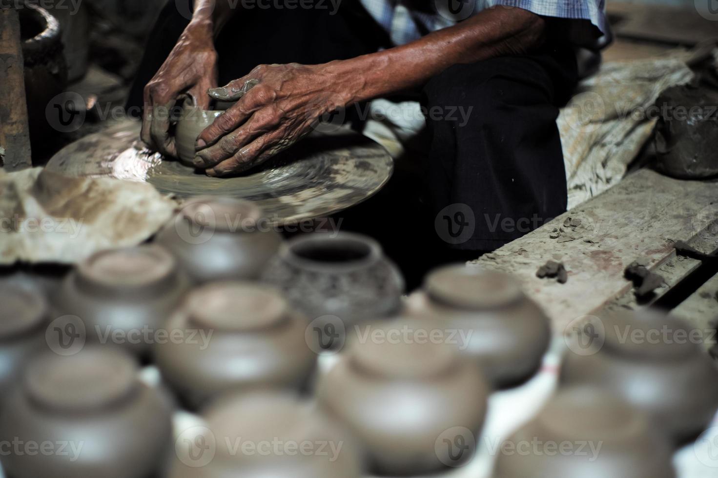 sélectif concentré sur la peau ridée sale mains du vieil homme moulant le travail d'argile sur le rouet pour faire le pot avec un groupe flou de pots d'argile au premier plan photo