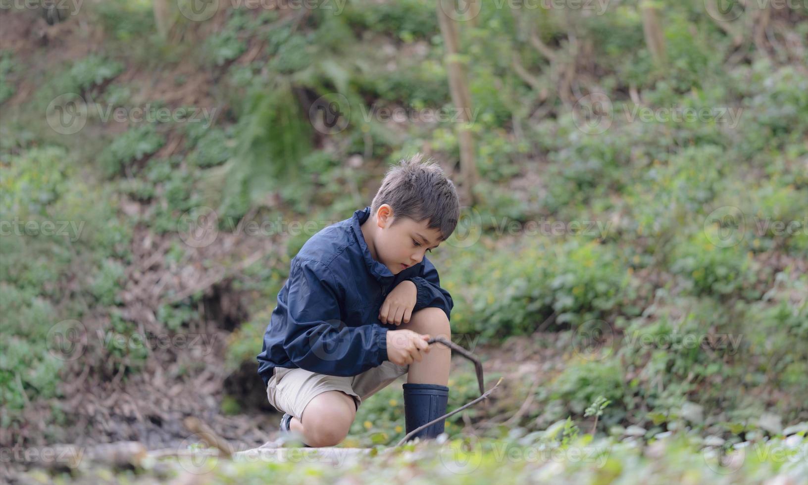 heureux jeune garçon jouant en plein air dans le jardin, portrait enfant assis sur une marche tenant un bâton en bois aime jouer dehors le matin, enfant se détendre le printemps ou l'été ensoleillé dans le parc forestier. photo