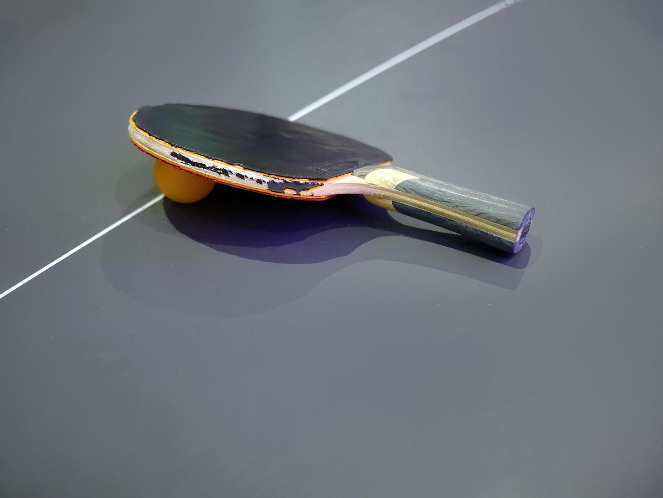 vue en grand angle d'une batte et d'une balle de tennis de table délabrées sur une table de couleur sombre photo