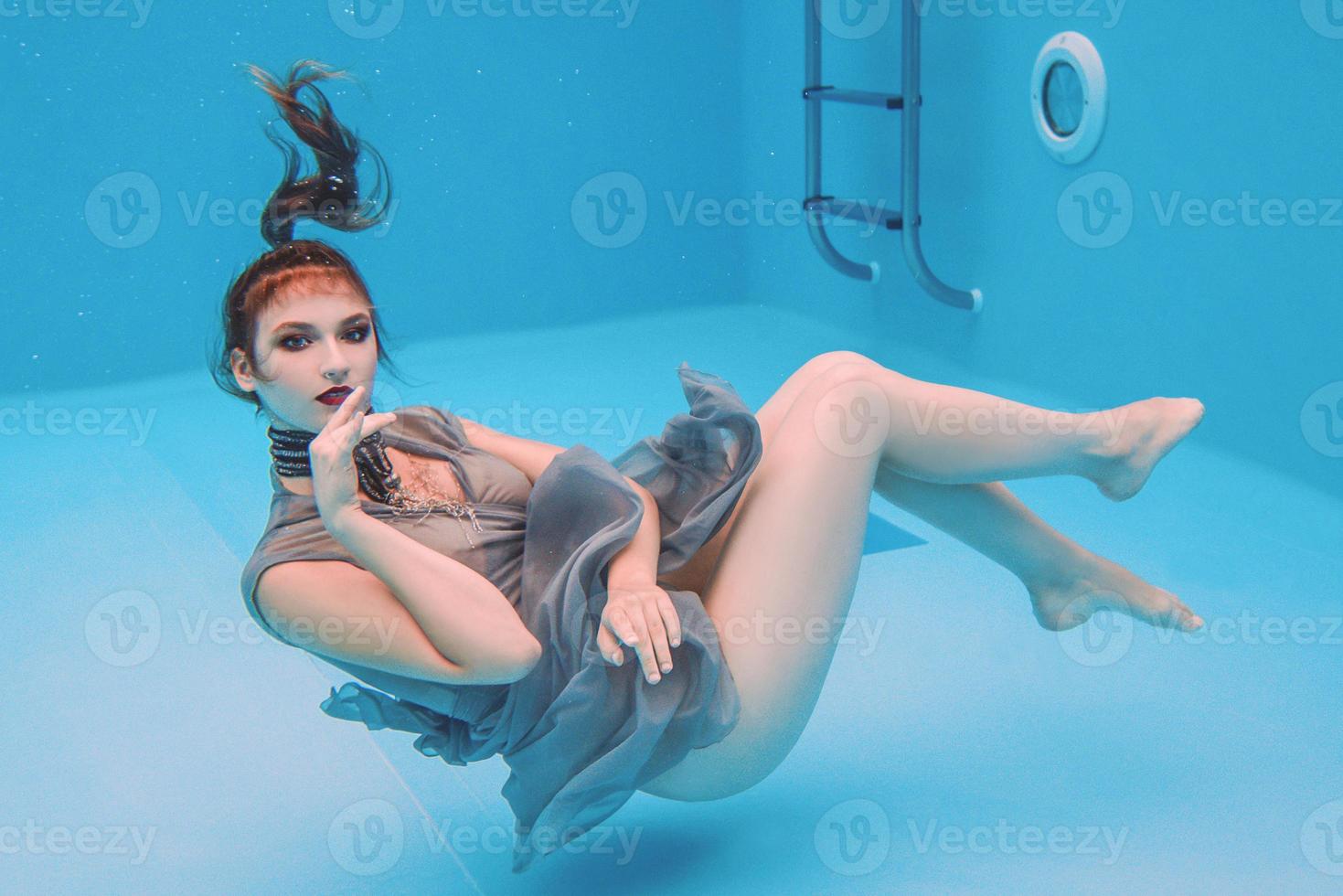 portrait d'art surréaliste de jeune femme en robe grise et foulard perlé sous l'eau dans la piscine photo