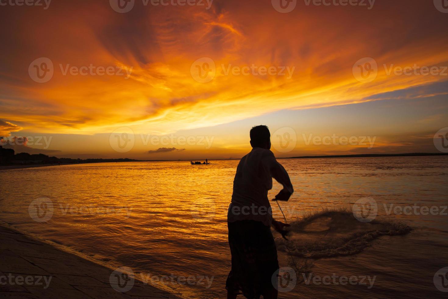 un pêcheur attrapant du poisson en mer contre le ciel orange au coucher du soleil photo