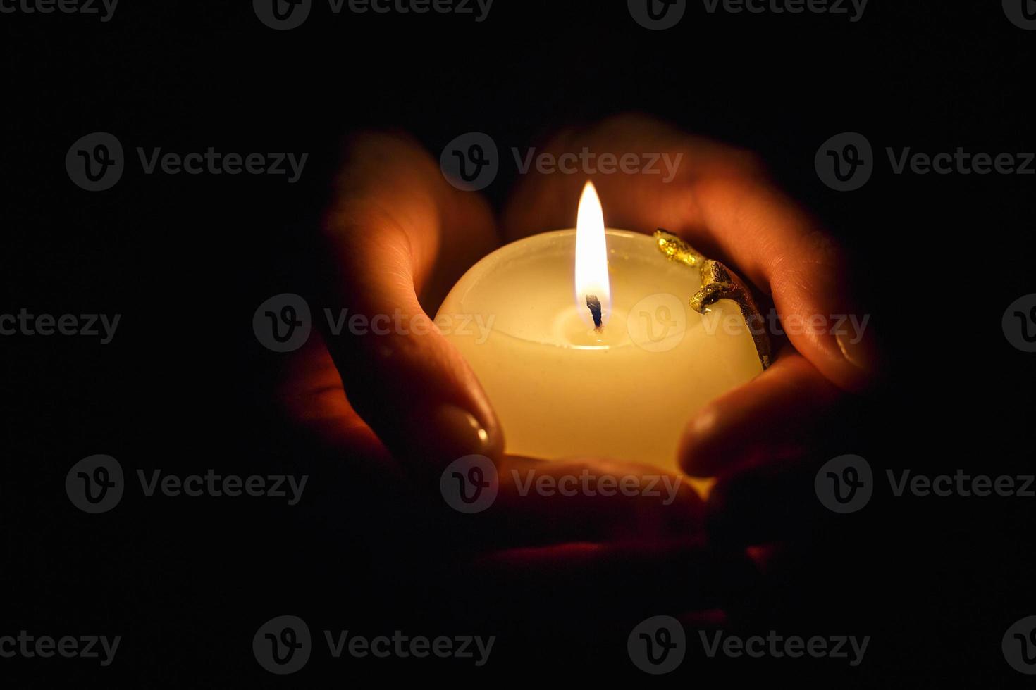bougie allumée dans les mains d'une fille en prière sur fond noir photo