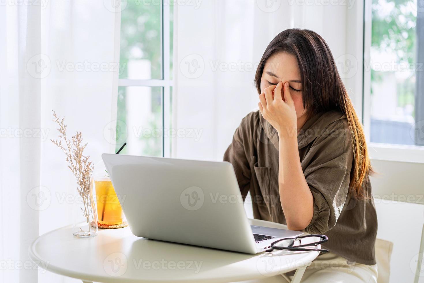 fatiguée et stressée, une jeune femme asiatique ressent de la douleur la fatigue oculaire et se frotte les yeux et enlève ses lunettes alors qu'elle est assise sur son lieu de travail photo