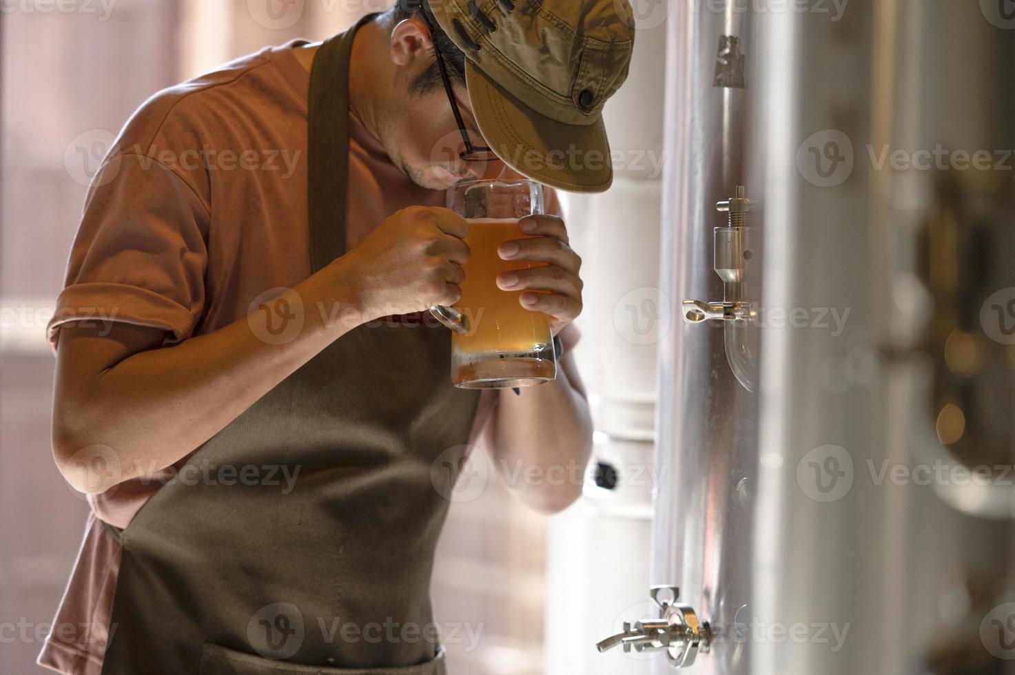 un jeune homme travaille dans une brasserie et vérifie la qualité de la bière artisanale. le propriétaire de la brasserie déguste les meilleures bières de bach. le raccourci d'un homme remplit un verre de bière avec photo