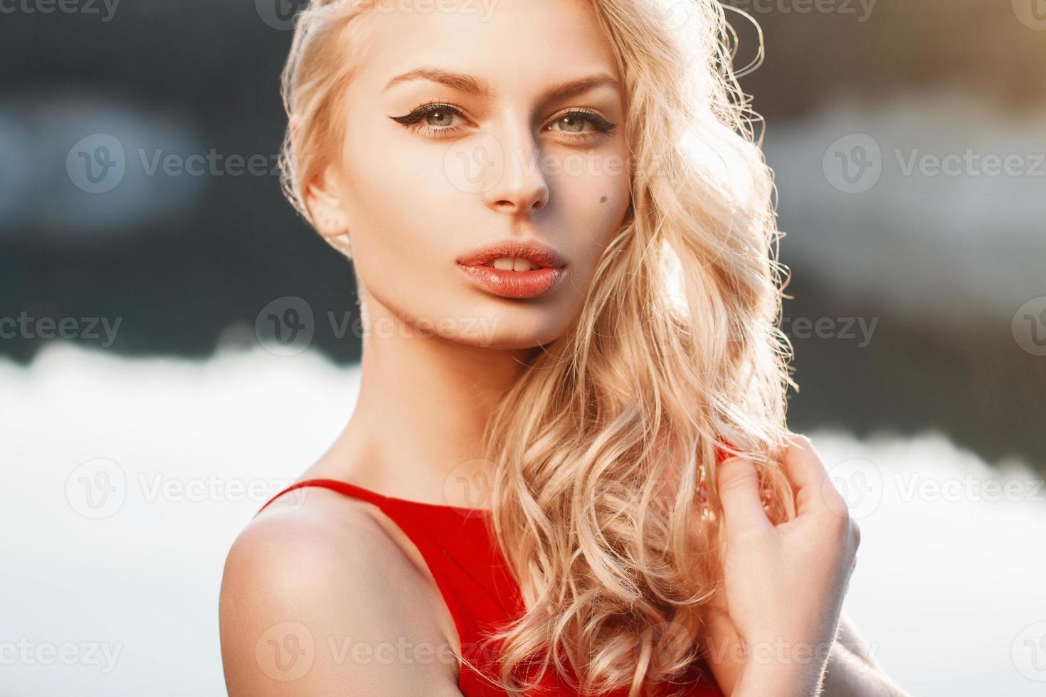 portrait en gros plan d'une belle femme avec une robe rouge sur le fond de la mer. lumière du coucher du soleil photo