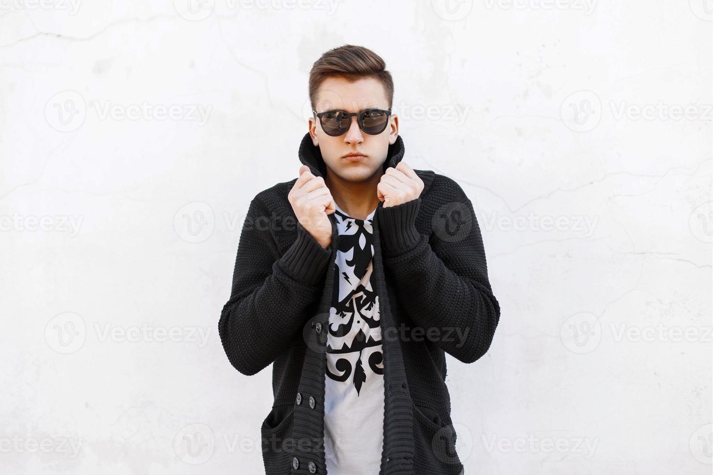 jeune bel homme à lunettes de soleil et un pull sur fond blanc. photo