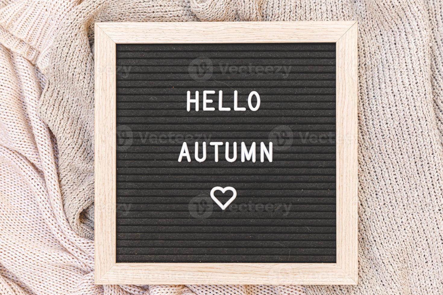 fond automnal. tableau à lettres noir avec phrase de texte bonjour automne allongé sur un pull en tricot blanc. vue de dessus, mise à plat. bannière d'action de grâces. concept de temps froid d'humeur hygge photo