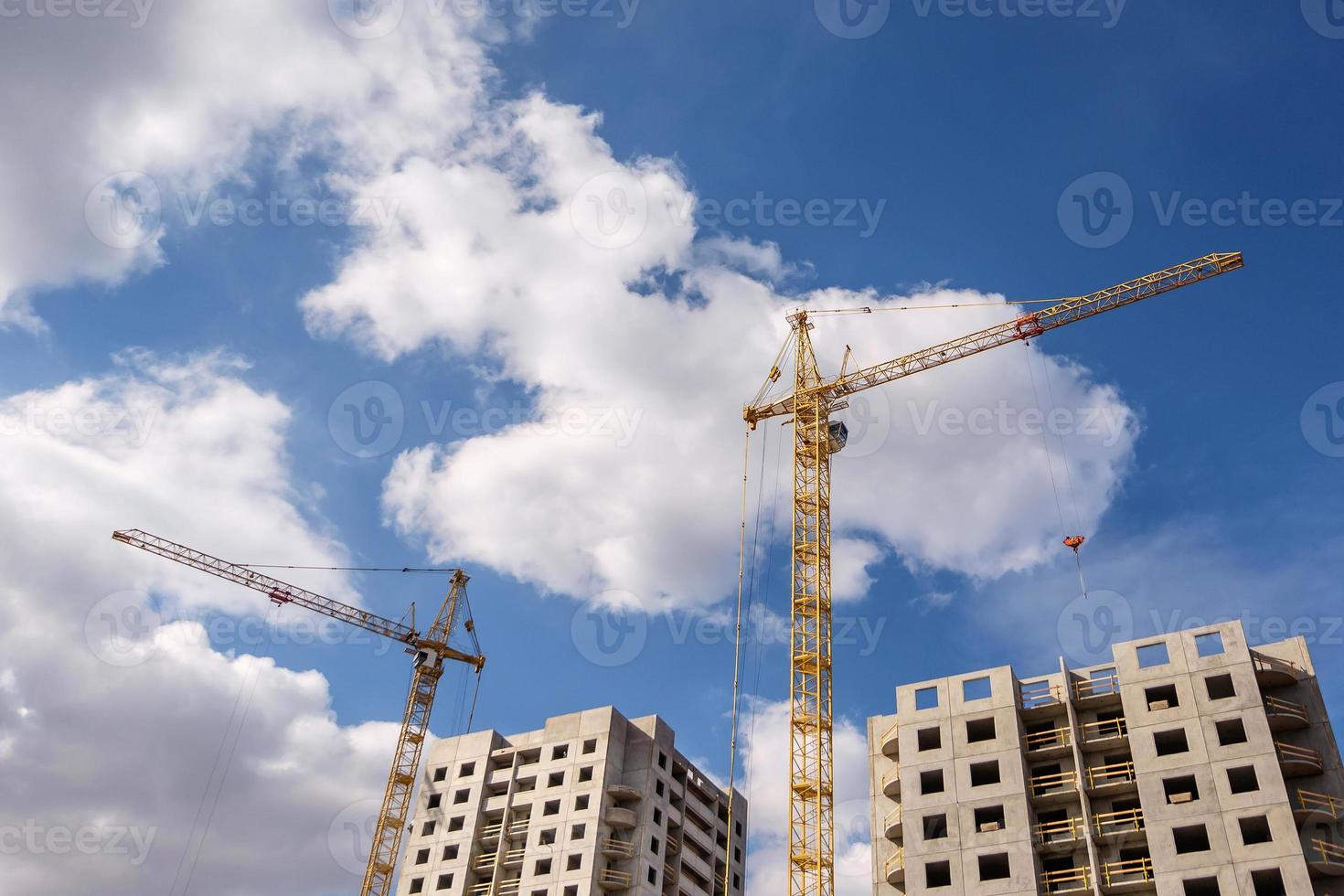 grues à tour et immeubles de plusieurs étages inachevés près des bâtiments en construction le jour ensoleillé avec de beaux nuages photo