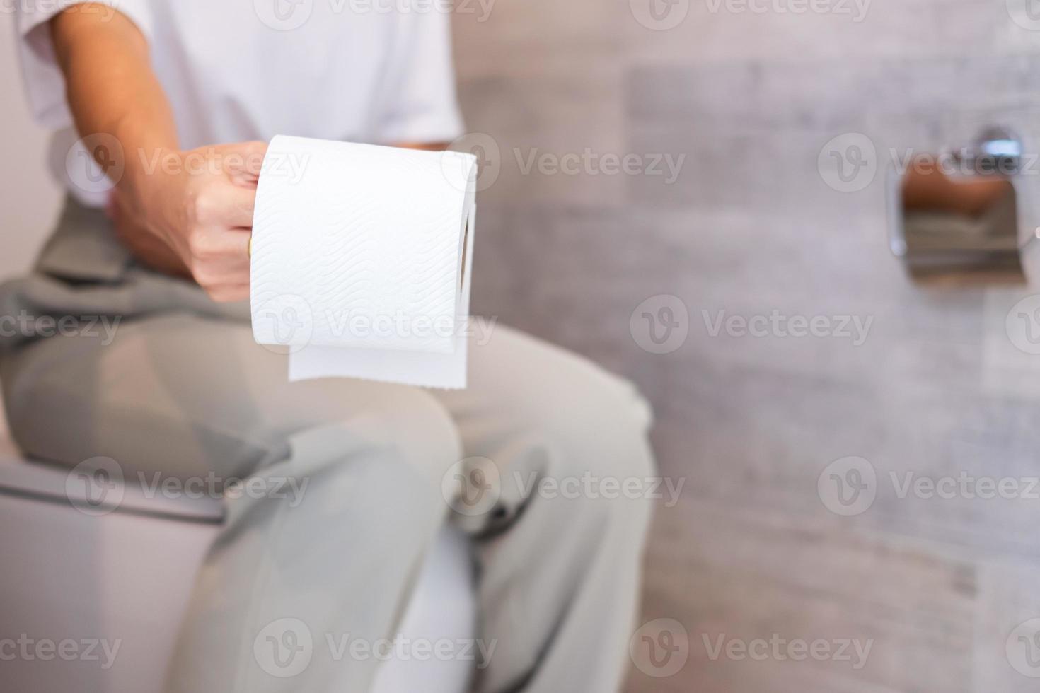 femme tenant un rouleau de papier toilette pendant s'asseoir sur la cuvette des toilettes. diarrhée, période de constipation, infection, abdominale, maux d'estomac, cystite, assurance et concept médical photo