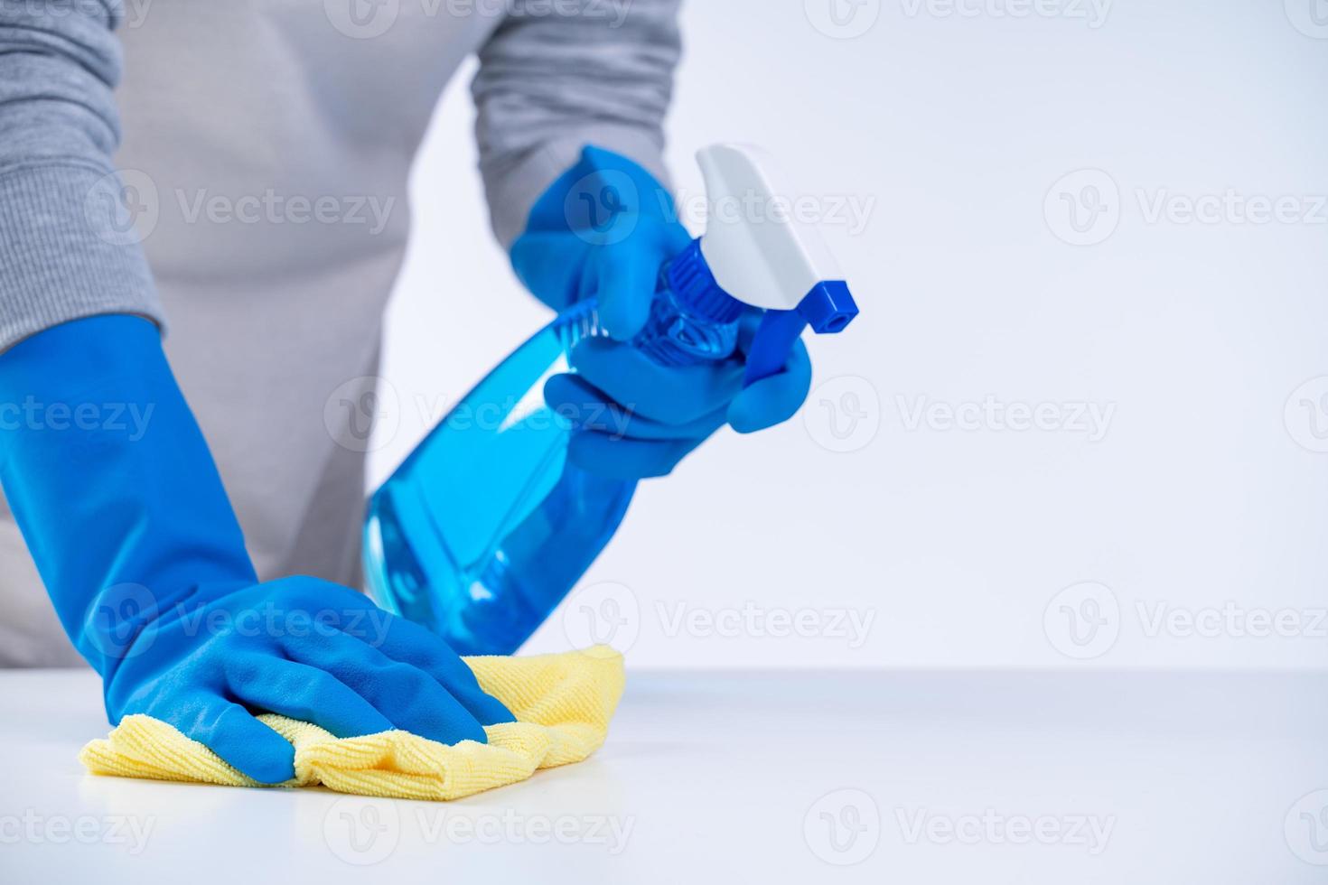 femme de ménage utilisant un chiffon et un flacon pulvérisateur pour nettoyer la surface de la table. photo