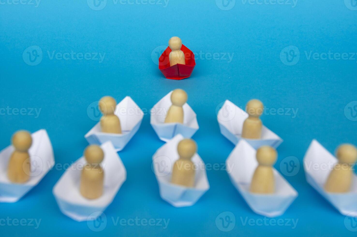 concept de leadership - figure en bois sur l'origami du navire en papier rouge menant le reste de la figure sur le navire en papier blanc. photo