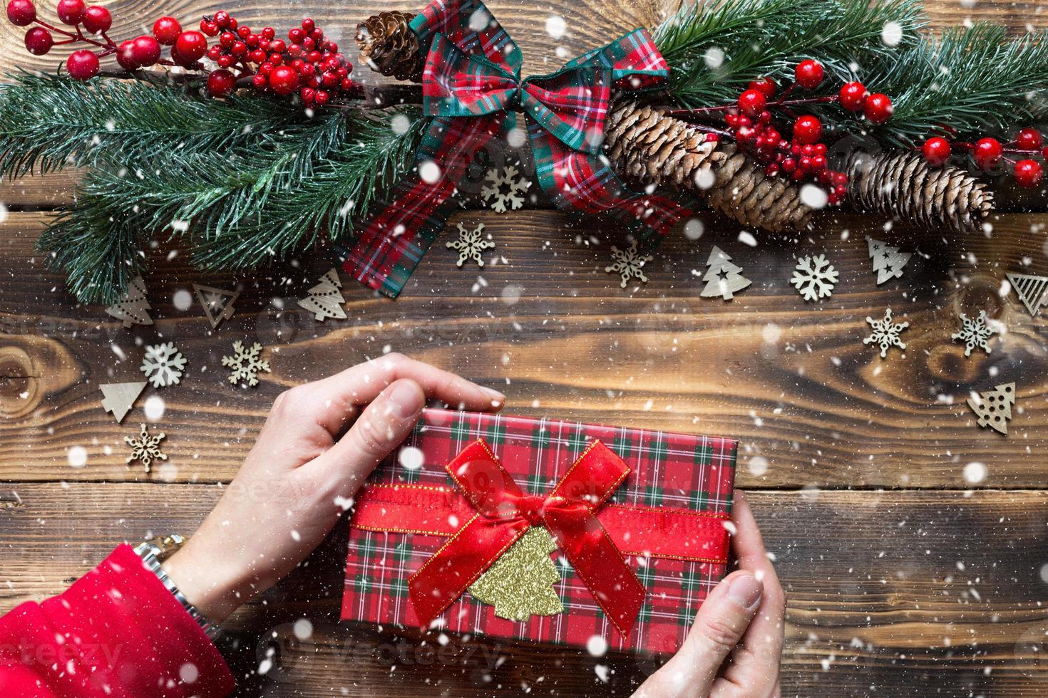 mains tenant une boîte-cadeau sur un fond de noël en bois. nouvel an, ambiance de vacances, sapin de noël, flocons de neige, cônes. copyspace, respectueux de l'environnement, mise à plat. emballage de vacances photo