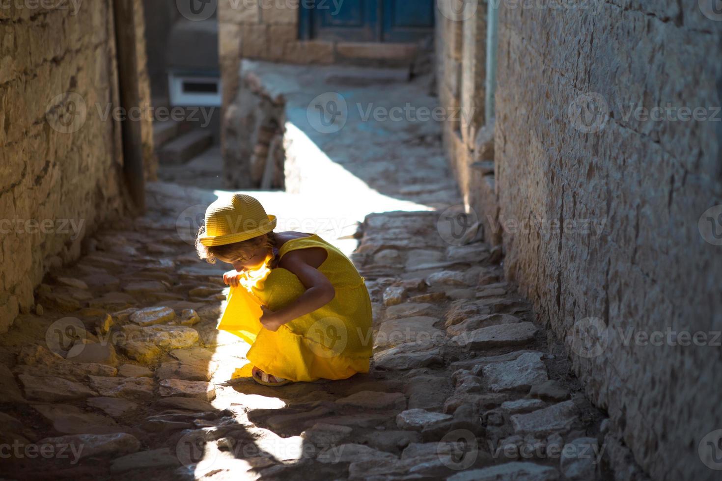 une touriste portant un chapeau jaune et une robe d'été se promène dans la rue de la vieille ville en pierre avec une forteresse. visite guidée. l'enfant s'est perdu, cherchant ses parents photo