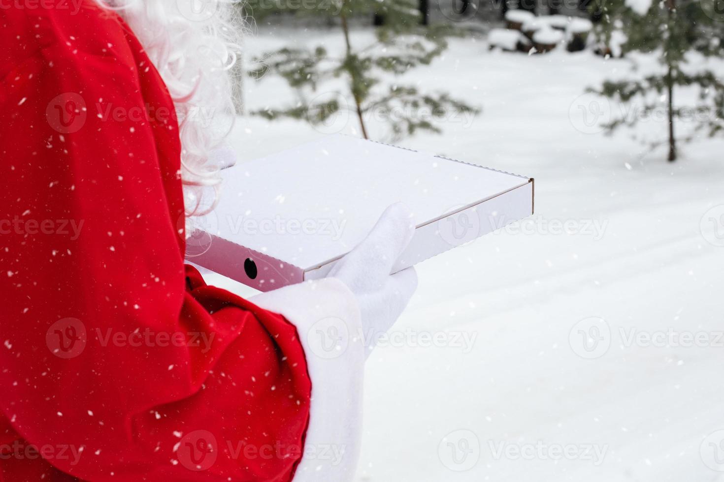 boîte à pizza blanche entre les mains du père noël en mitaines blanches, avec une barbe, en manteau rouge. livraison de restauration rapide de Noël. promotion du nouvel an. travailler sur la restauration des jours fériés. espace de copie, maquette photo