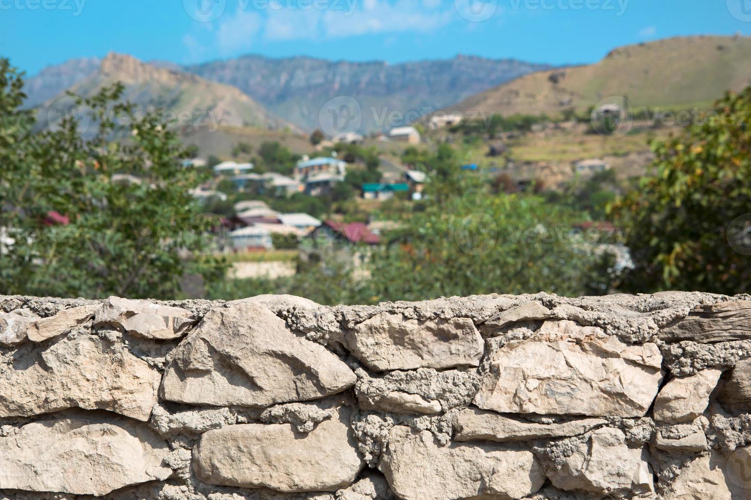 murs en pierre de maçonnerie de premier plan naturel avec en arrière-plan un village de montagne avec des maisons et des arbres en défocalisation. tourisme, écologie, thème écologique photo