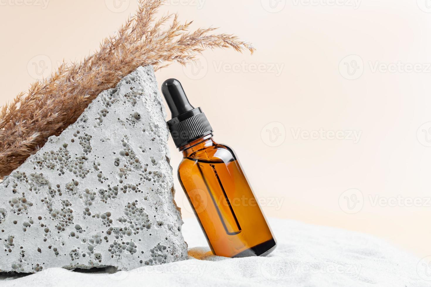 bouteille de sérum marron en verre avec une pipette pour les soins de la peau sur le sable avec des pierres et des roseaux secs. le concept de santé et de beauté. minimalisme, espace de copie photo