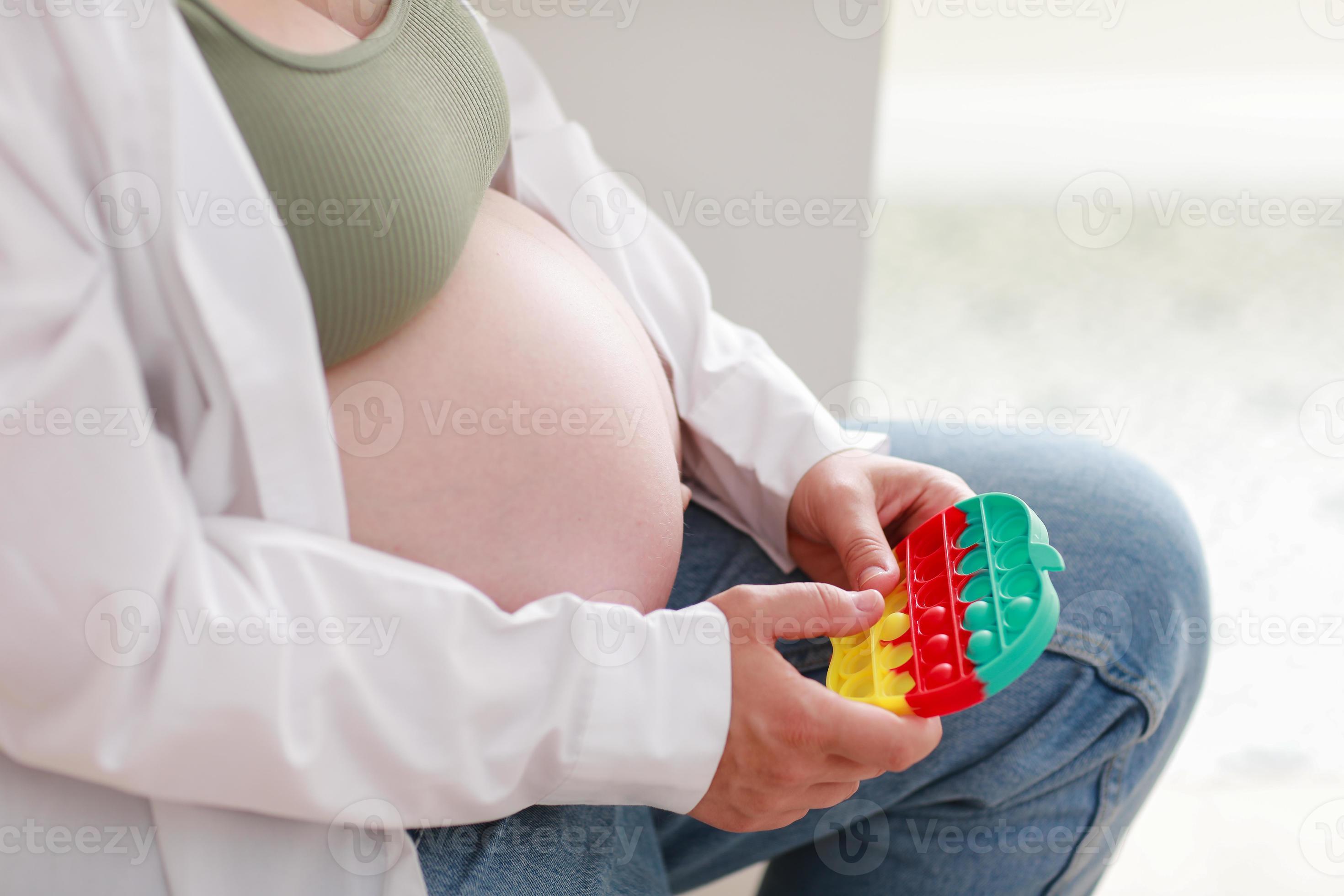 une femme enceinte avec un gros ventre de grossesse avancée utilise un  jouet sensoriel pop it. fille appuie sur des bulles de silicone colorées.  soulagement du stress et de l'anxiété. jeu d'agitation
