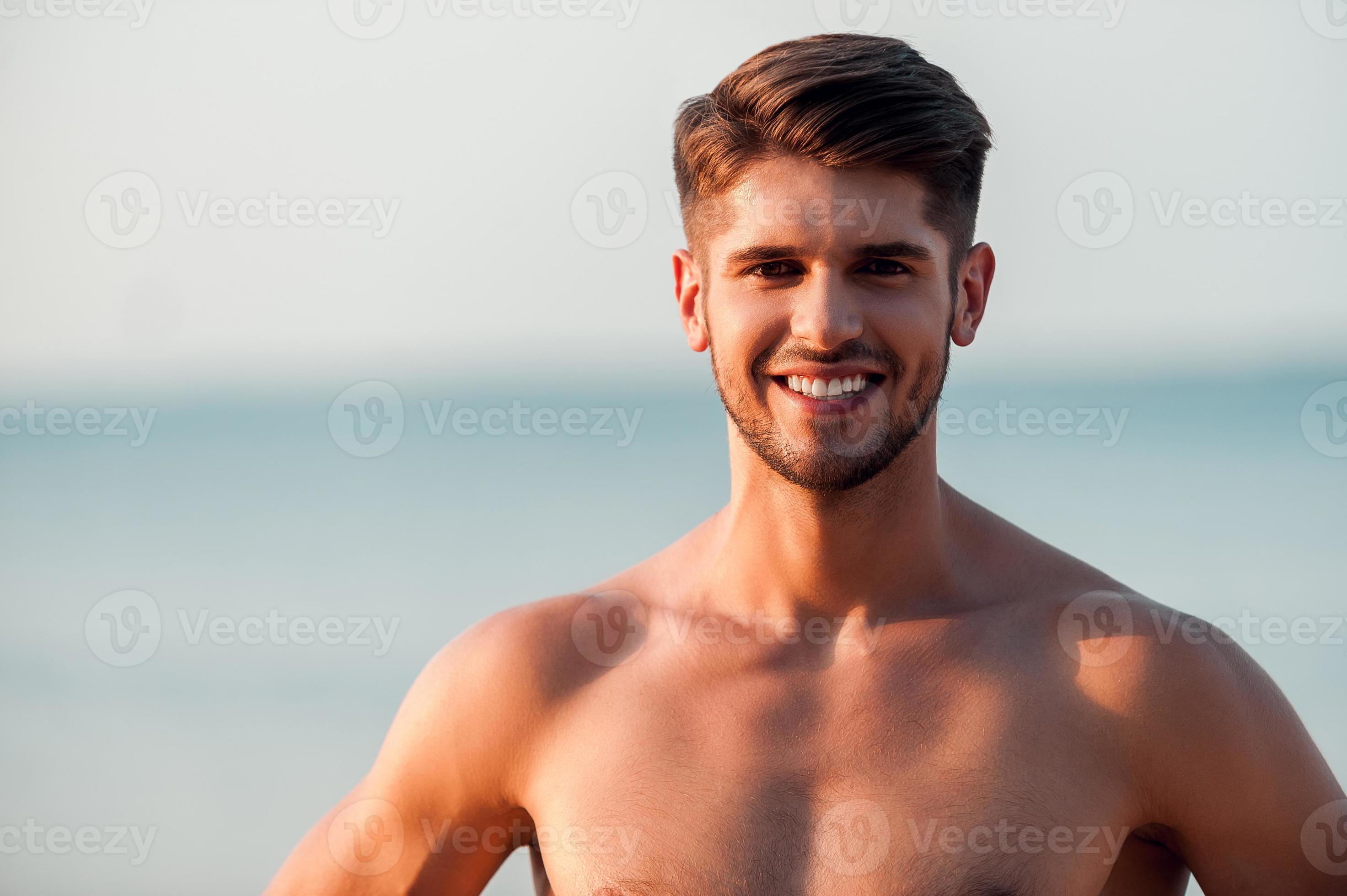 beau torse nu. heureux jeune homme musclé regardant la caméra et