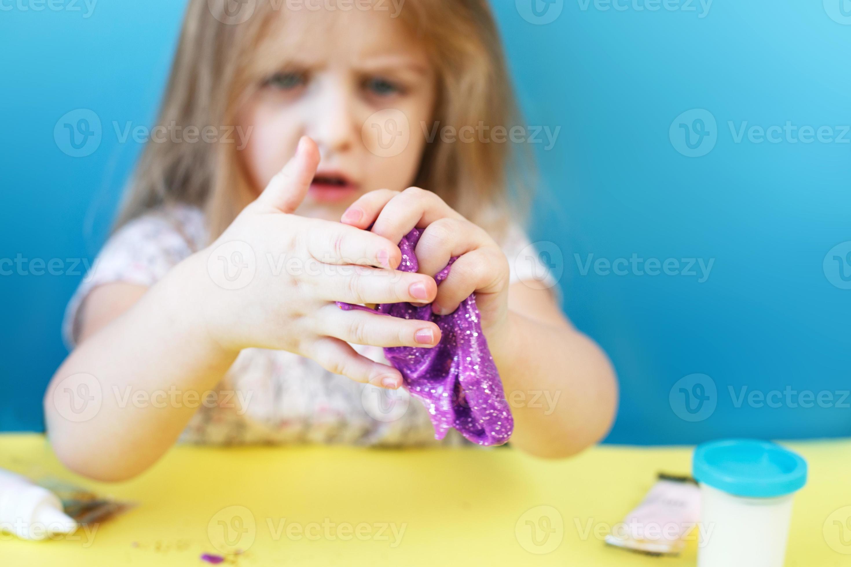 fille blonde tenir slime violet isolé sur fond bleu. enfant jouant avec un  jouet visqueux. faire de la boue. espace de copie. 14001808 Photo de stock  chez Vecteezy