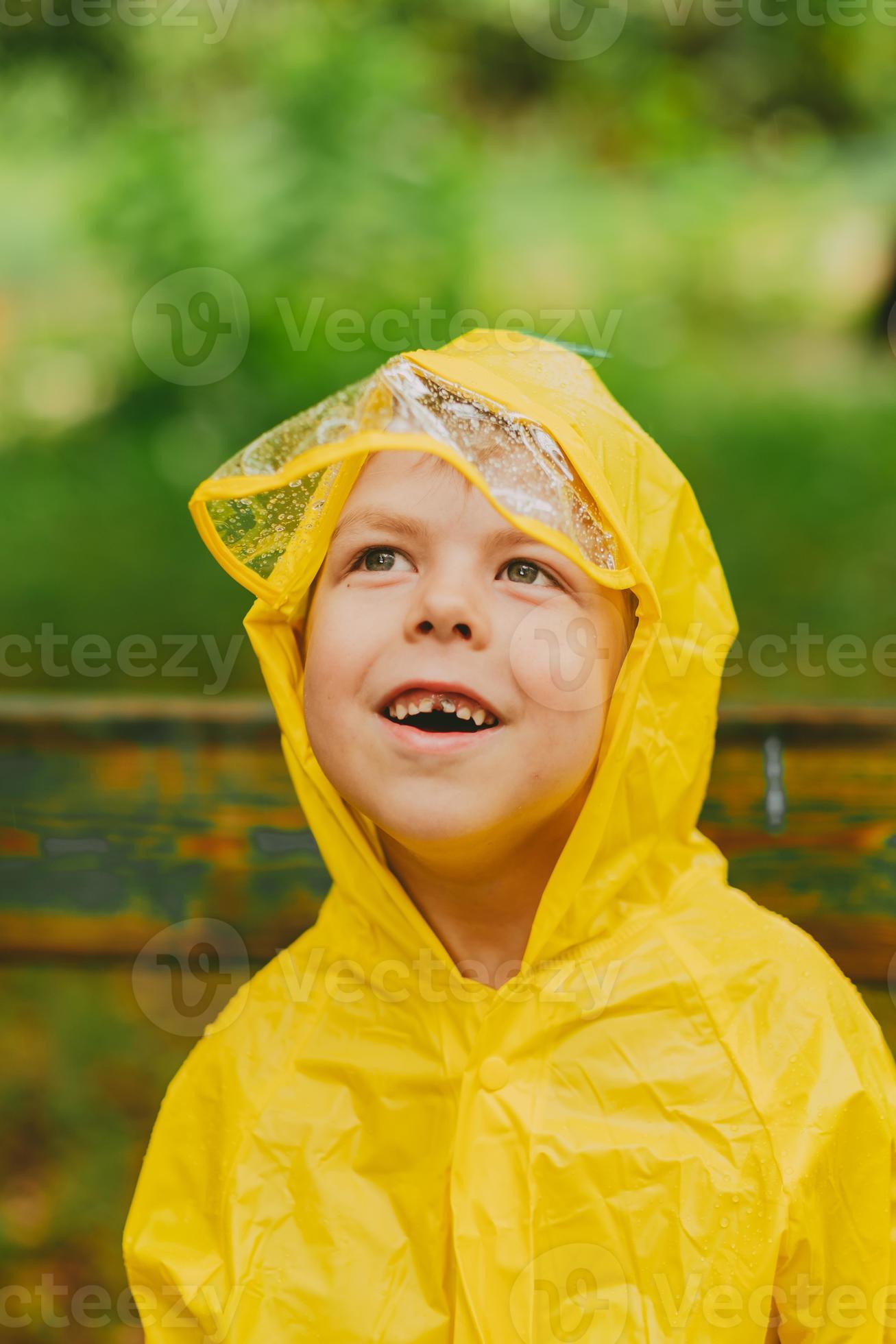 portrait d'un garçon dans un imperméable jaune dans la rue pendant la pluie.  protection contre la pluie. gouttes de pluie sur une cagoule transparente  couvrant le visage. vêtements lumineux pour les enfants